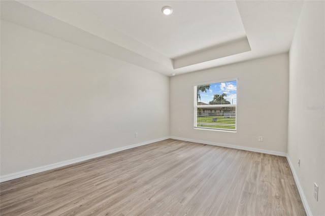 unfurnished room with a tray ceiling and light wood-type flooring