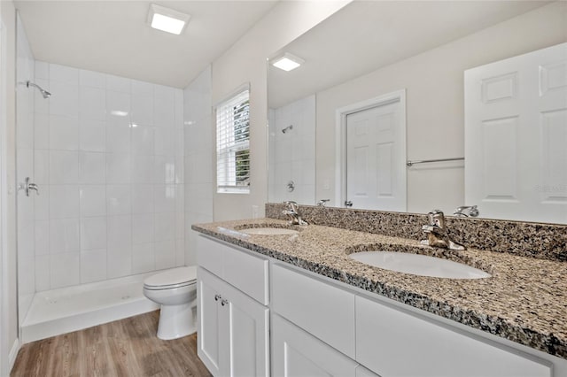 bathroom featuring a tile shower, vanity, wood-type flooring, and toilet