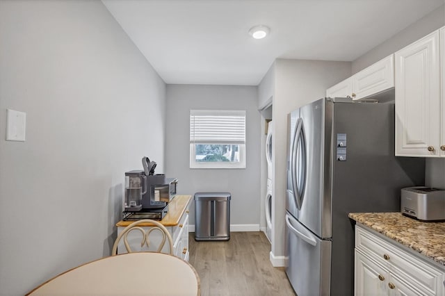 kitchen featuring stacked washer and dryer, light stone countertops, light wood-type flooring, white cabinets, and stainless steel refrigerator