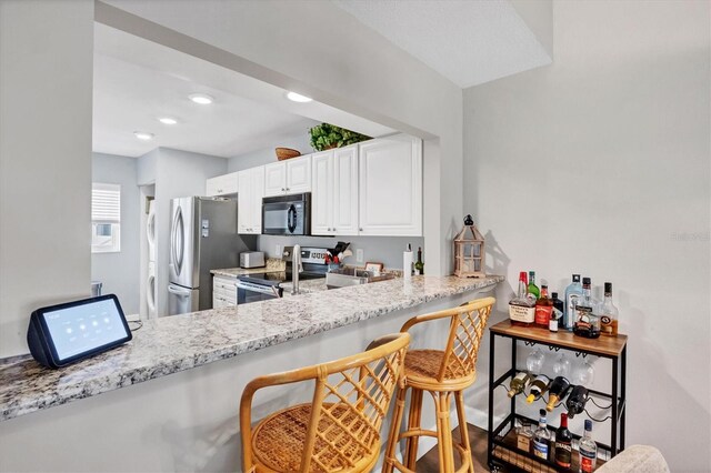 kitchen with kitchen peninsula, a breakfast bar, white cabinets, appliances with stainless steel finishes, and light stone counters