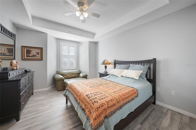 bedroom with hardwood / wood-style floors, ceiling fan, and a raised ceiling