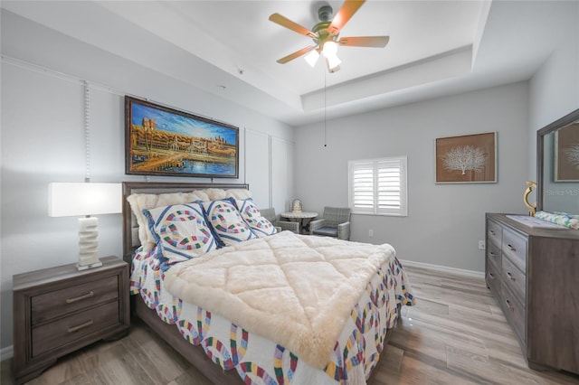 bedroom featuring light wood-type flooring, ceiling fan, and a raised ceiling