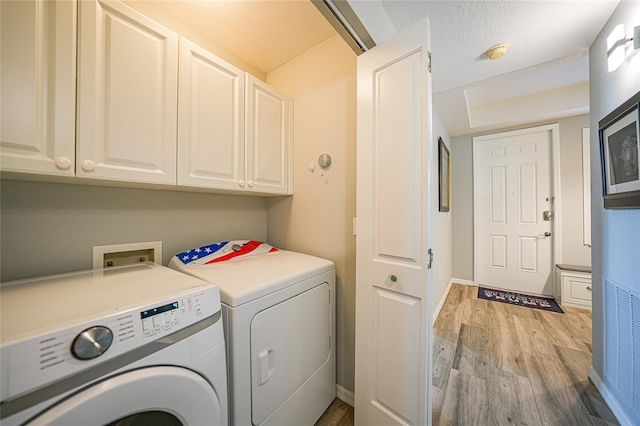 laundry room with washing machine and dryer, cabinets, and light hardwood / wood-style flooring