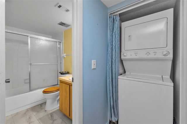 interior space featuring toilet, vanity, stacked washer and clothes dryer, and combined bath / shower with glass door