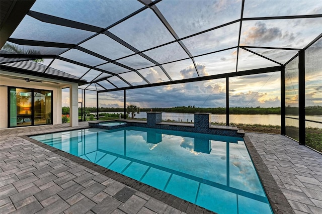 pool at dusk with a patio, a water view, a lanai, and an in ground hot tub