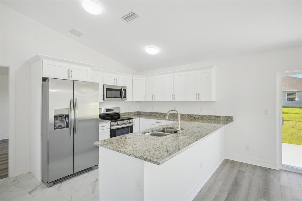 kitchen with kitchen peninsula, white cabinetry, vaulted ceiling, sink, and stainless steel appliances