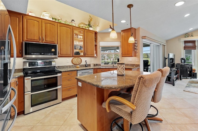 kitchen featuring light stone counters, vaulted ceiling, a breakfast bar area, a kitchen island, and appliances with stainless steel finishes