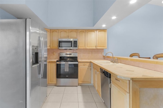 kitchen with kitchen peninsula, stainless steel appliances, sink, light tile patterned floors, and light brown cabinetry