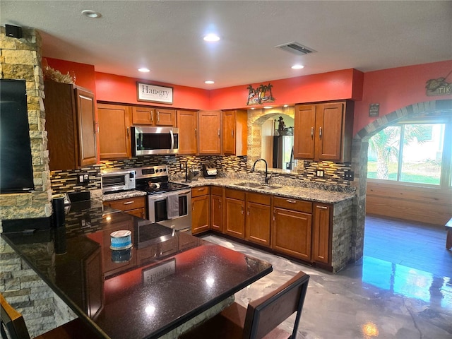 kitchen featuring hardwood / wood-style flooring, backsplash, dark stone countertops, sink, and appliances with stainless steel finishes