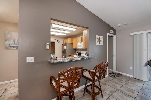 kitchen featuring light brown cabinets, lofted ceiling, light tile patterned flooring, and white appliances