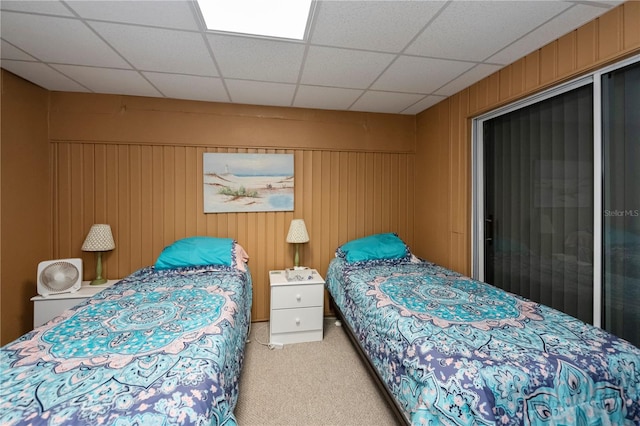 bedroom with a paneled ceiling, light colored carpet, and wood walls