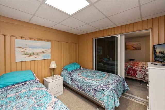 carpeted bedroom featuring a drop ceiling and wood walls