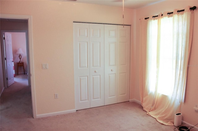 unfurnished bedroom featuring multiple windows, light carpet, and a closet