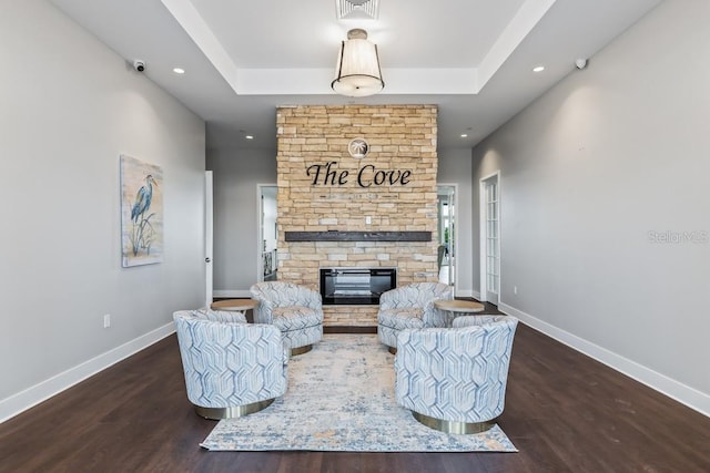 living area with a fireplace, visible vents, dark wood finished floors, baseboards, and a raised ceiling