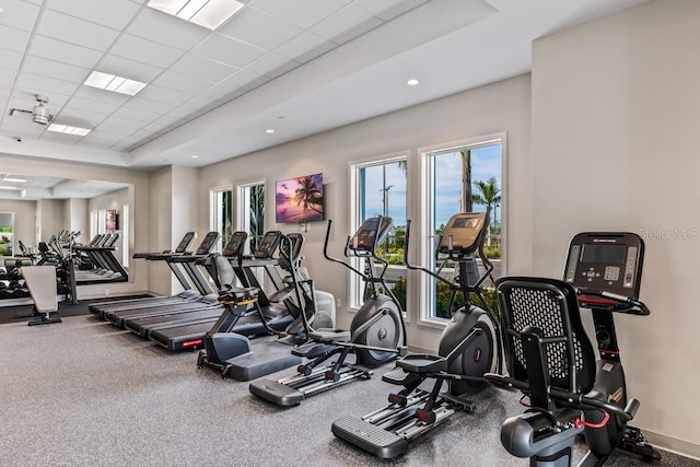 gym with a raised ceiling, a paneled ceiling, and baseboards