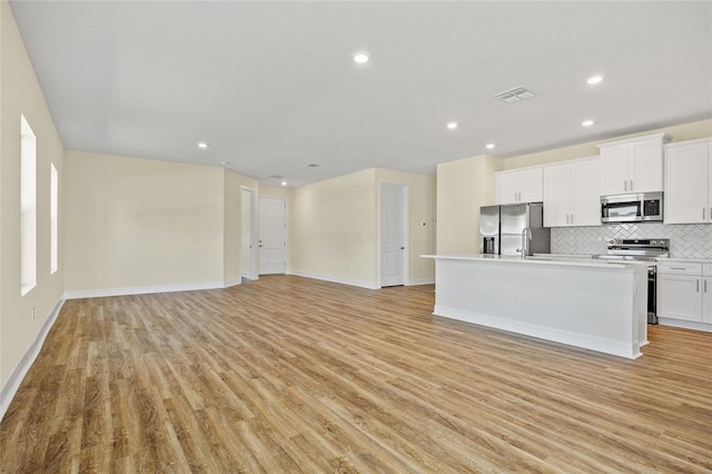 1293 Preston St, Port Charlotte, FL 33952 - kitchen featuring appliances with stainless steel finishes, backsplash, light wood-style flooring, open floor plan, and white cabinetry