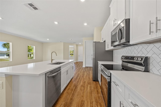 1293 Preston St, Port Charlotte, FL 33952 - kitchen featuring appliances with stainless steel finishes, an island with sink, light wood-style flooring, light countertops, and backsplash