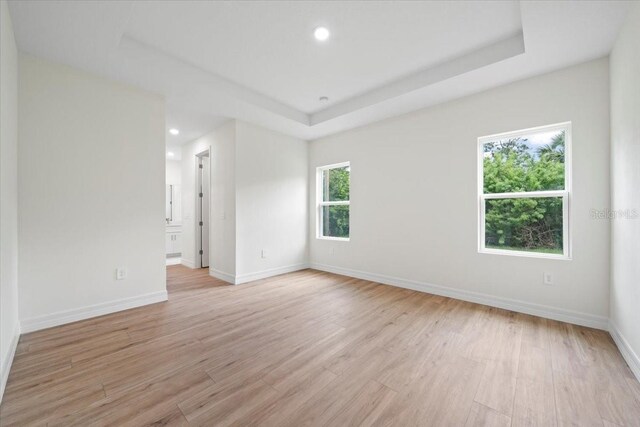 empty room featuring light wood-type flooring, baseboards, and a raised ceiling