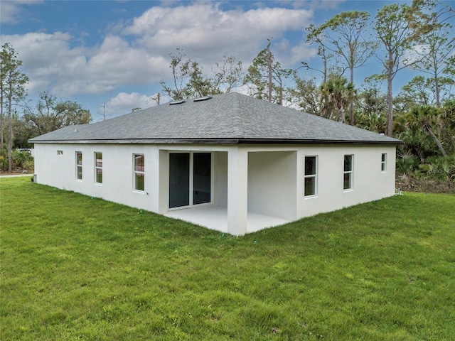 rear view of house with roof with shingles, a patio, and a yard