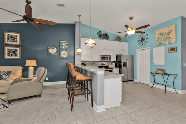 kitchen featuring white cabinetry, stainless steel appliances, kitchen peninsula, decorative light fixtures, and a breakfast bar area