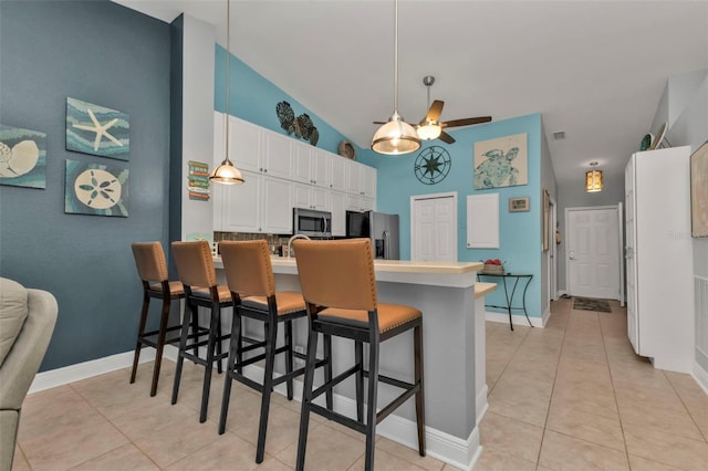 kitchen featuring white cabinetry, stainless steel appliances, pendant lighting, a kitchen bar, and light tile patterned floors