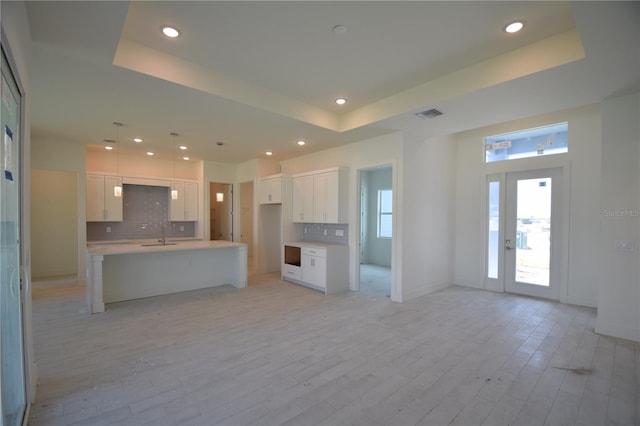 kitchen featuring a center island with sink, white cabinets, a tray ceiling, and light hardwood / wood-style floors