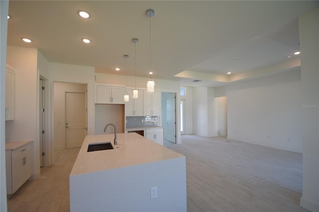 kitchen with sink, hanging light fixtures, white cabinetry, light hardwood / wood-style floors, and a kitchen island with sink