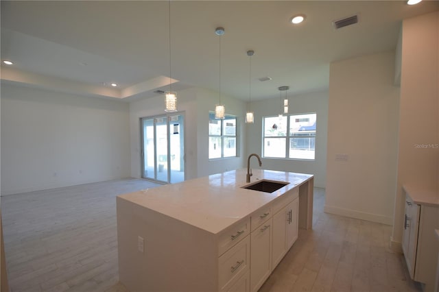 kitchen with an island with sink, sink, decorative light fixtures, light wood-type flooring, and white cabinets