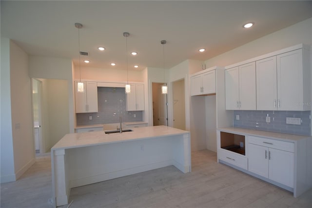 kitchen featuring decorative backsplash, white cabinets, hanging light fixtures, light wood-type flooring, and sink