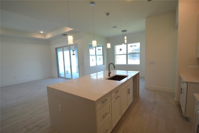 kitchen with light wood-type flooring, sink, an island with sink, and hanging light fixtures