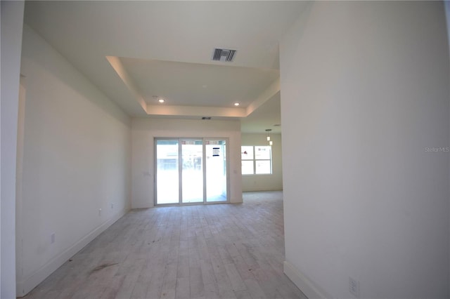 empty room featuring a tray ceiling and light hardwood / wood-style flooring