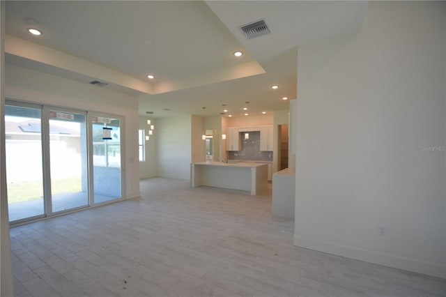 unfurnished living room with light hardwood / wood-style floors and a tray ceiling