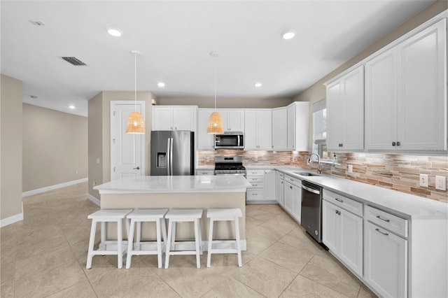 kitchen featuring white cabinets, decorative backsplash, a kitchen island, pendant lighting, and appliances with stainless steel finishes