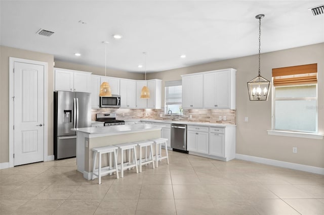 kitchen with stainless steel appliances, tasteful backsplash, a center island, white cabinets, and pendant lighting