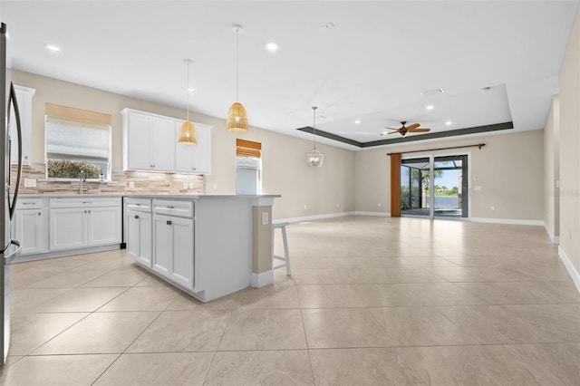 kitchen with a kitchen island, hanging light fixtures, decorative backsplash, white cabinets, and a tray ceiling