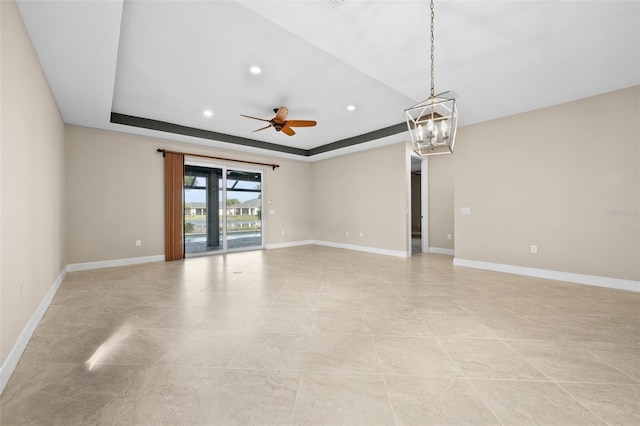 spare room featuring ceiling fan with notable chandelier and a raised ceiling