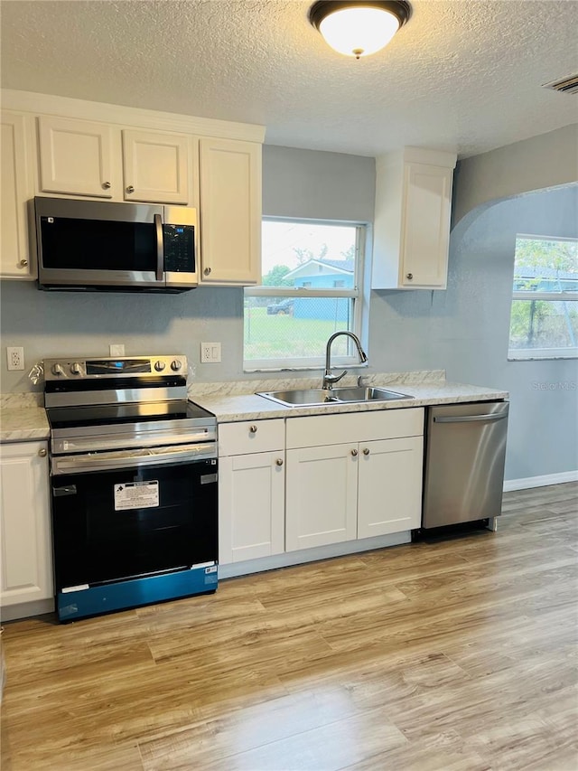 kitchen featuring white cabinets, sink, light wood-type flooring, a textured ceiling, and stainless steel appliances