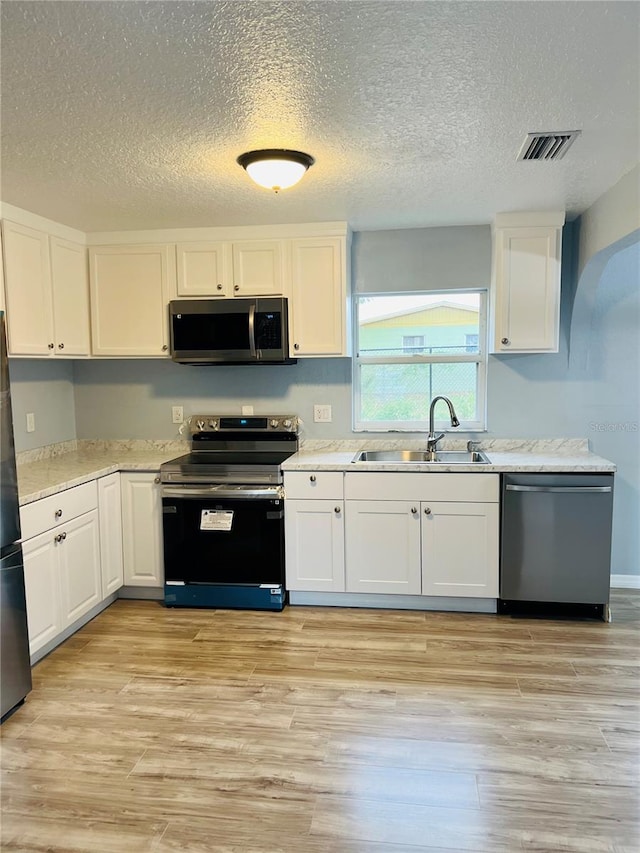 kitchen featuring a textured ceiling, stainless steel appliances, sink, light hardwood / wood-style flooring, and white cabinetry