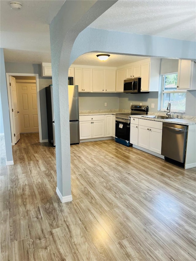 kitchen featuring white cabinetry, sink, light wood-type flooring, and appliances with stainless steel finishes