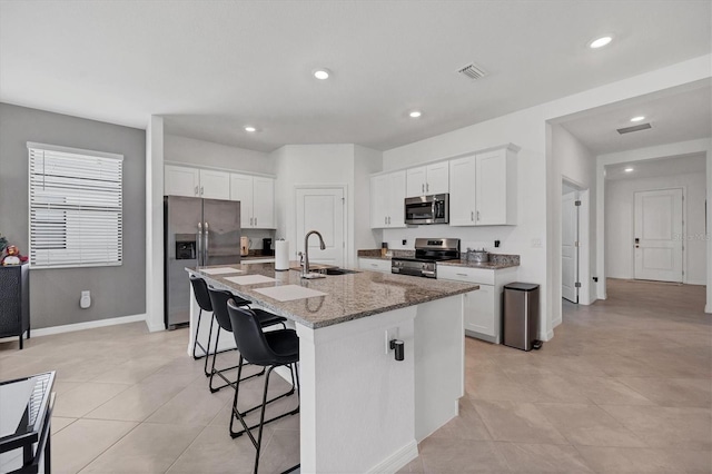 kitchen featuring white cabinets, an island with sink, appliances with stainless steel finishes, light stone countertops, and sink