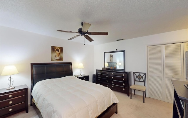 bedroom featuring ceiling fan, a closet, light colored carpet, and a textured ceiling