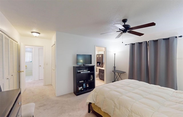 bedroom with light carpet, ensuite bath, a textured ceiling, ceiling fan, and multiple closets