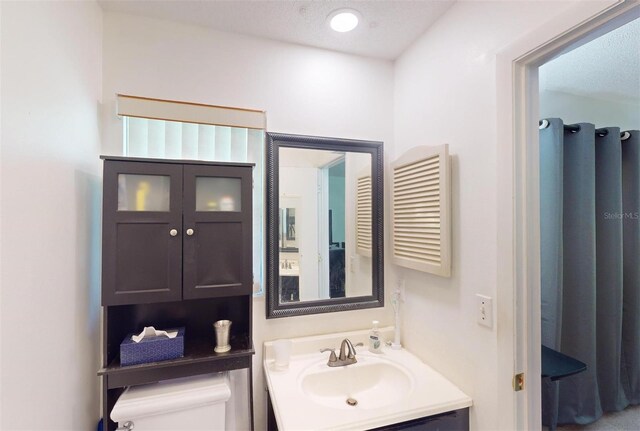 bathroom with a textured ceiling, vanity, and toilet