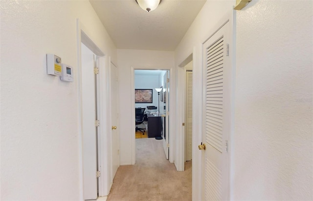 hallway with a textured ceiling and light colored carpet