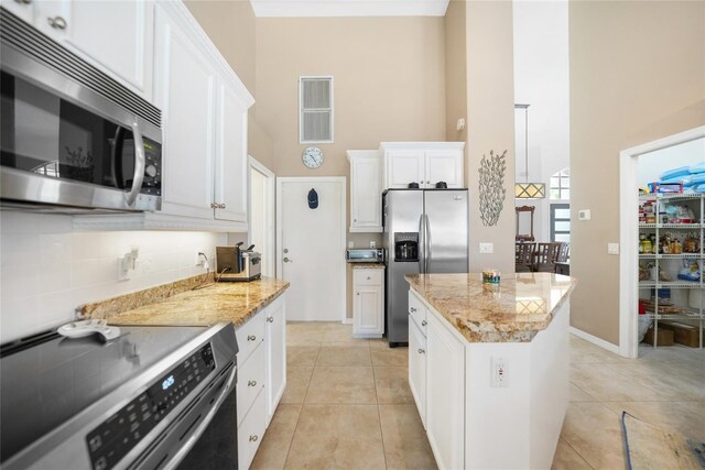 kitchen featuring white cabinets, appliances with stainless steel finishes, a kitchen island, and light stone countertops