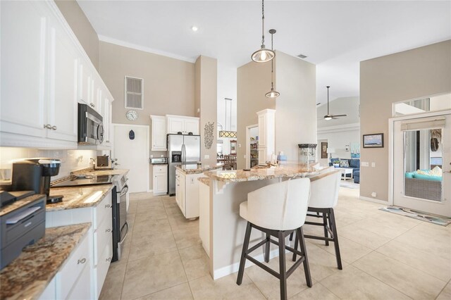 kitchen with stainless steel appliances, light stone counters, decorative light fixtures, a kitchen island, and white cabinets