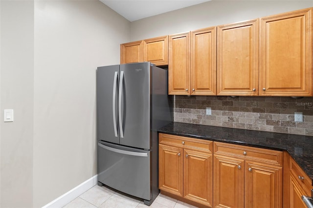 kitchen with dark stone countertops, tasteful backsplash, stainless steel refrigerator, and light tile patterned floors