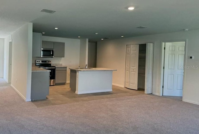 kitchen with a kitchen island with sink, gray cabinets, appliances with stainless steel finishes, and light colored carpet