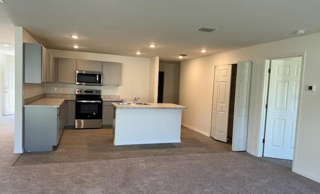 kitchen with dark carpet, a center island with sink, stainless steel appliances, gray cabinets, and sink