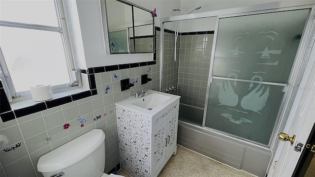 full bathroom with tile walls, shower / bath combination with glass door, toilet, and vanity